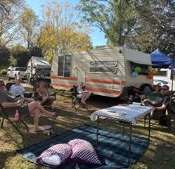 Friends sitting outside a caravan under shady trees at Imbil Camping Retreat